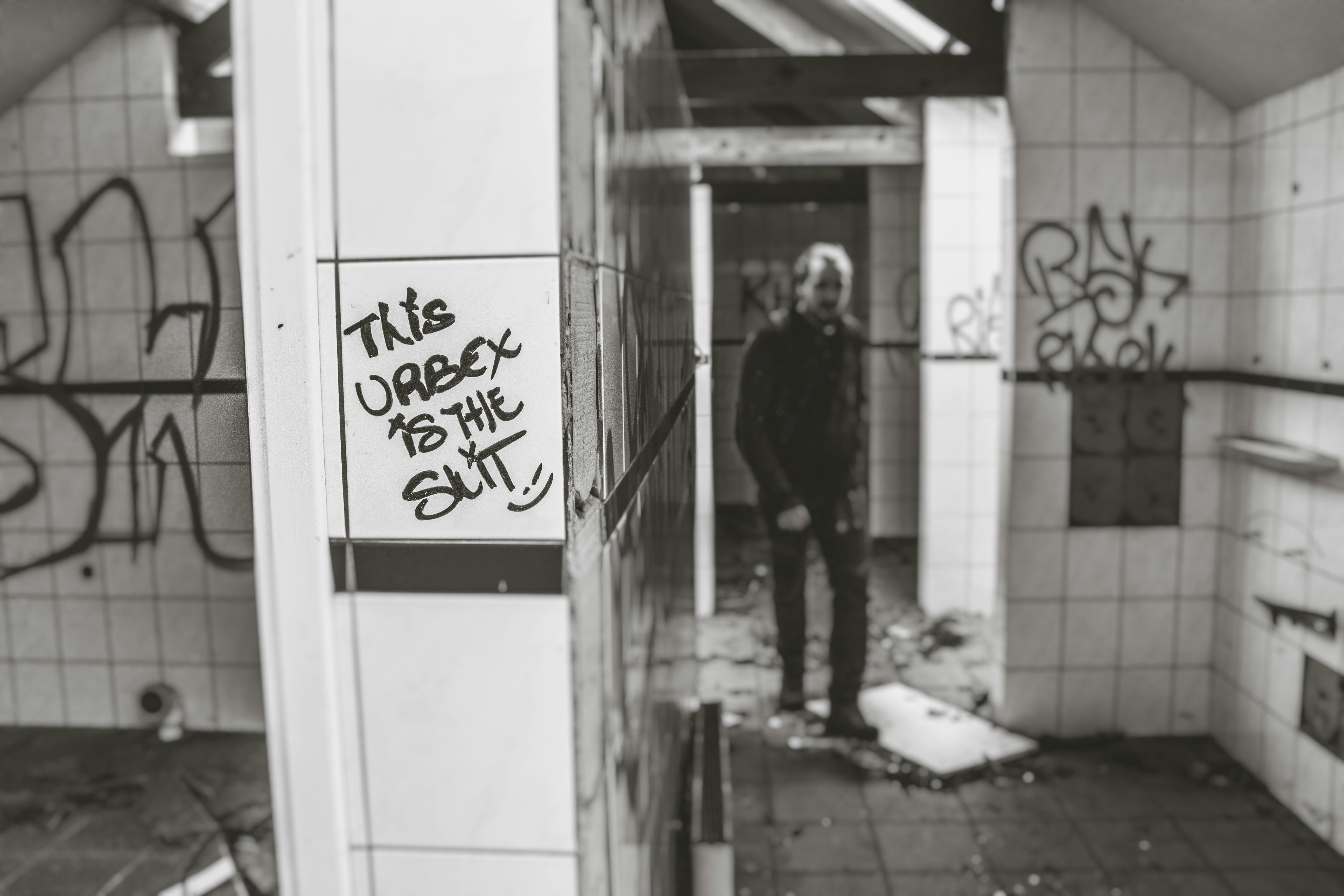 grayscale photo of man standing near white tile wall